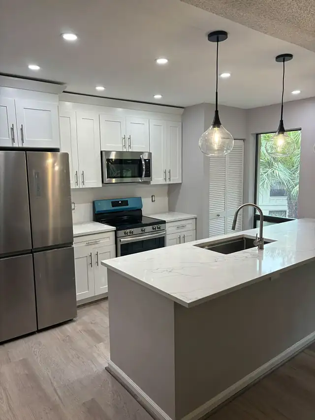 Kitchen renovation with white shaker cabinetry, quartz island and glass pendant lights