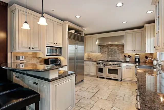 Kitchen with cream cabinetry to the ceiling, professional range in a stone surround and a granite peninsula
