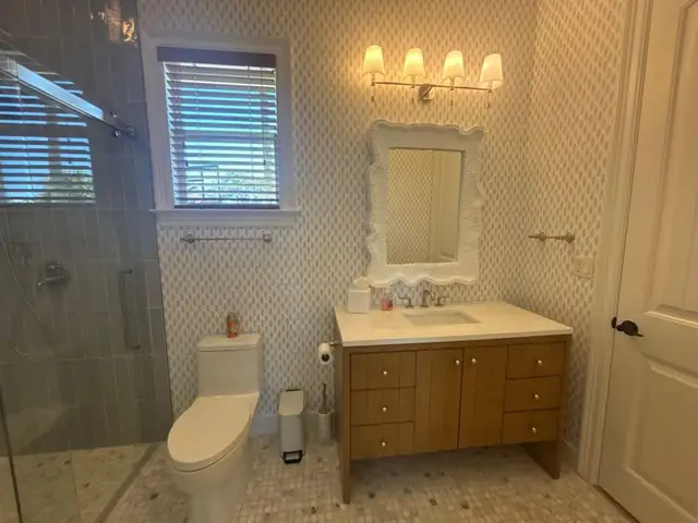 Guest bathroom with patterned wall tile, a wood vanity, a white framed mirror and a glass shower enclosure