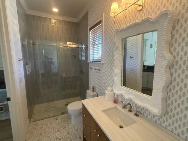 Guest bathroom with glass shower enclosure, dark vanity, ornate white mirror and patterned wall covering