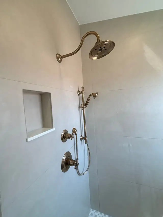 Walk-in shower with large-format tile, recessed niche and a brushed brass rain head and handheld