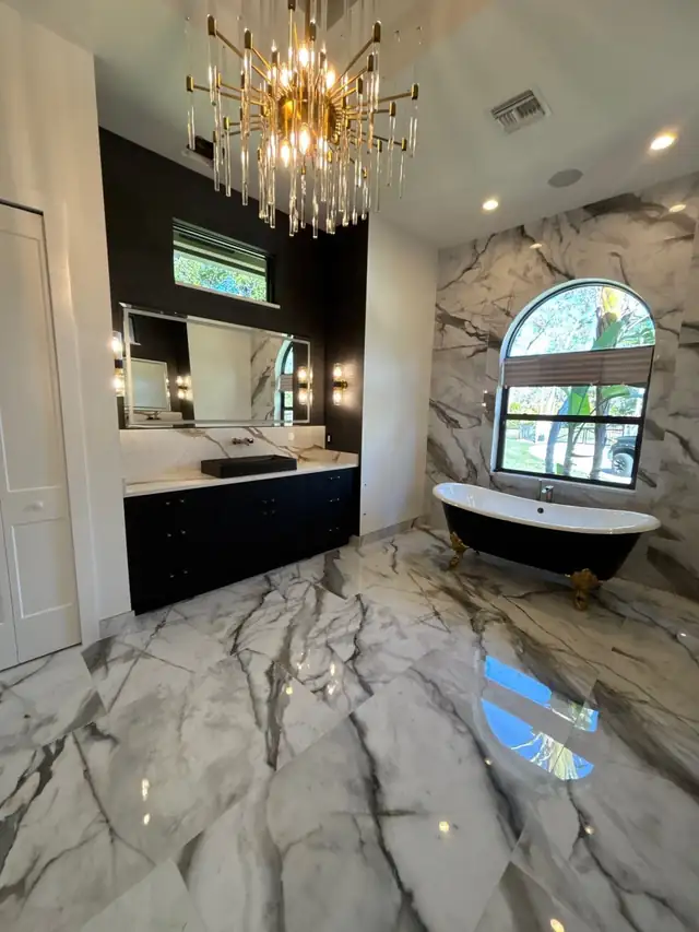 Primary bathroom with a black clawfoot tub, a book-matched marble wall and floor, a crystal chandelier and an arched window