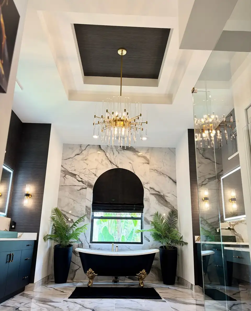 Primary bath by the bathroom remodeling Lake Worth Beach crew at H&H: black clawfoot tub, book-matched marble wall, navy double vanities and a brass chandelier in Wellington, FL