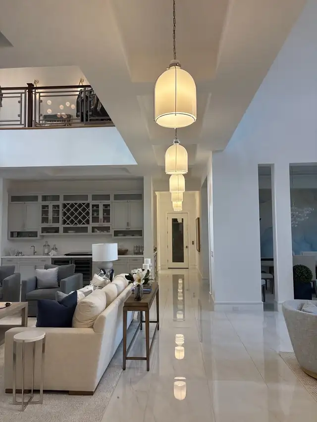 Open living area with white built-in bar cabinetry, wine storage and a row of glass pendant lights in a Palm Beach County home