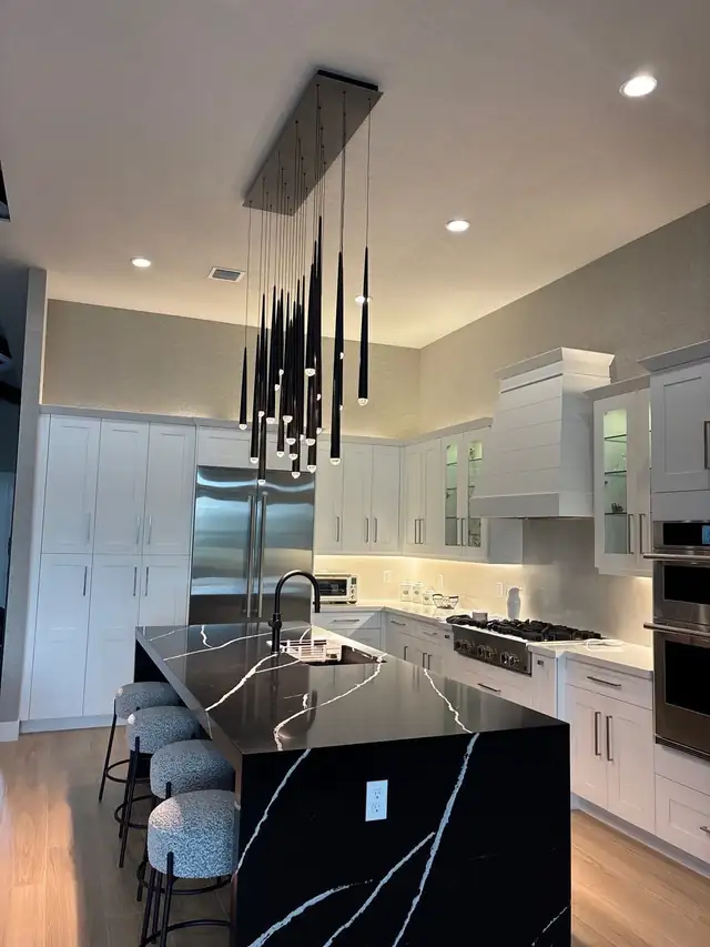 Kitchen remodel by H&H Signature Renovations with white cabinetry, a black marble-look island and a cluster of black pendant lights
