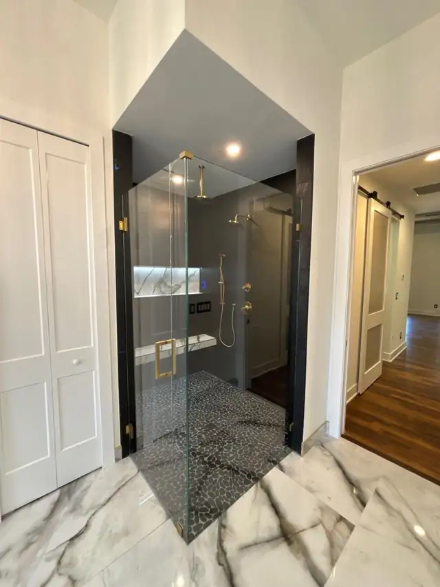 Frameless glass walk-in shower with marble tile and brass fixtures, built where an unused tub used to be