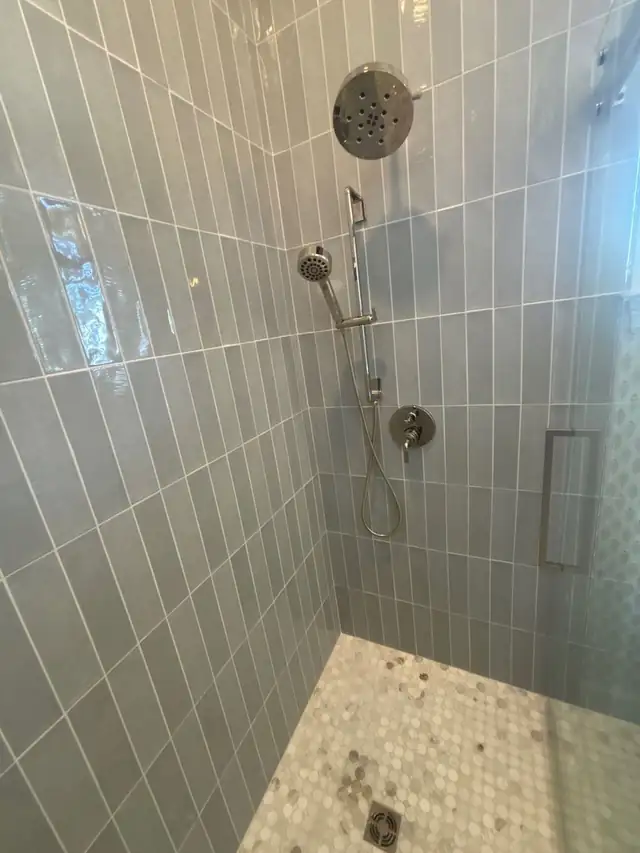 Walk-in shower with vertical stacked gray tile, mosaic floor and chrome shower system